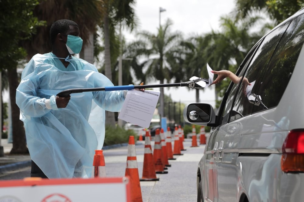 Healthcare worker Dante Hills, left, passes paperwork to a woman in a vehicle at a COVID-19 testing site outside of Marlins Park in Miami (AP Photo/Lynne Sladky)